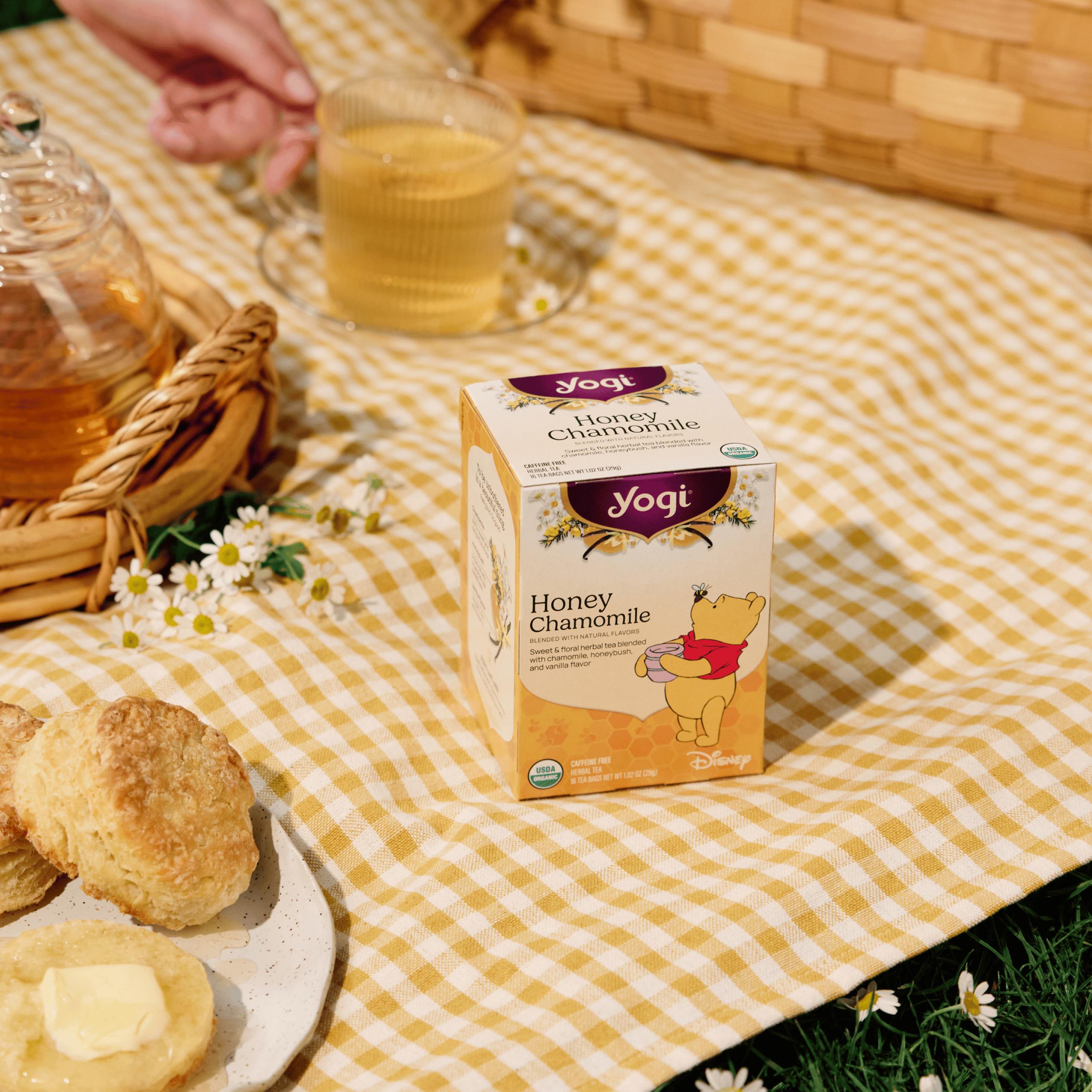 A sunny picnic scene on a yellow gingham blanket featuring Yogi Honey Chamomile and a hand reaching in for a mug of tea