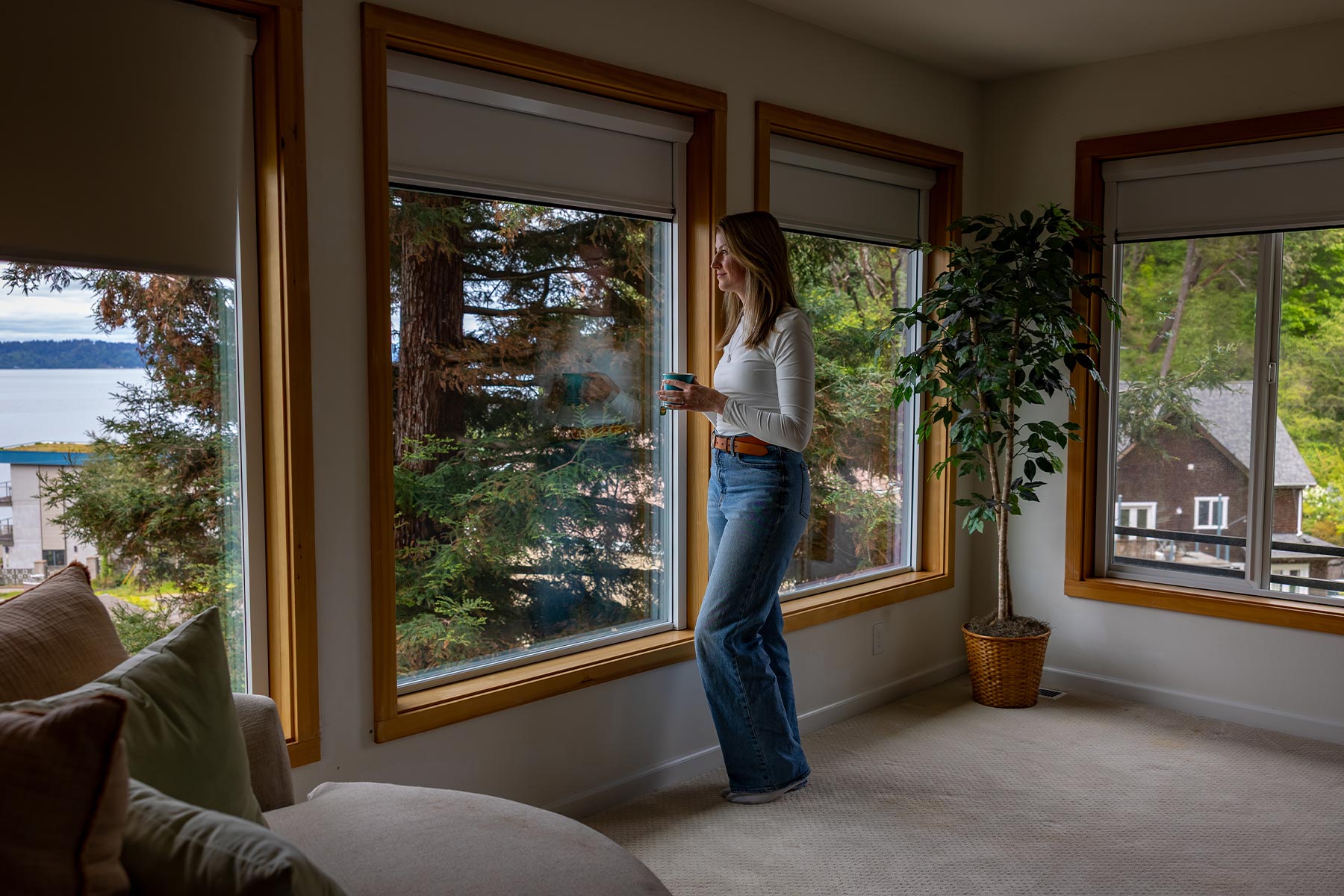 Woman standing by large windows with uBlockout roller shades partially lowered controlling daylight
