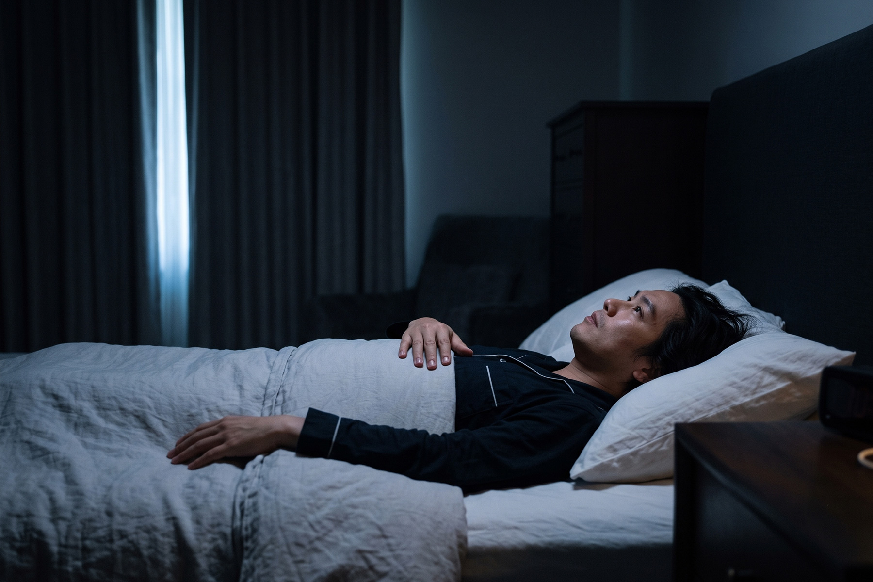 Person lying awake in a dark bedroom at night with faint light at the window edge