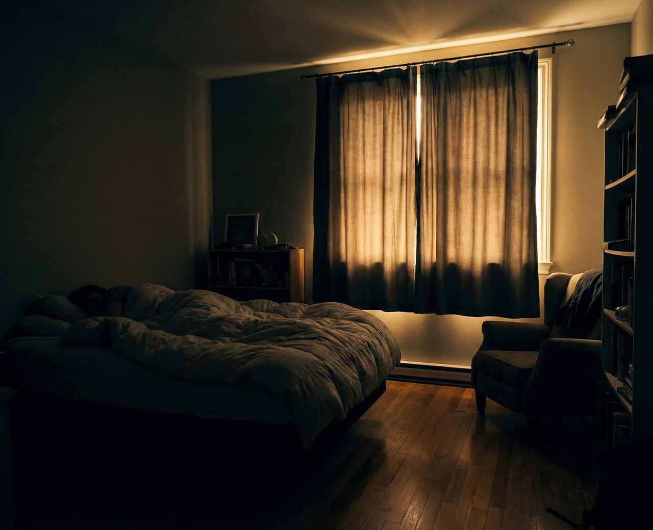 Person sleeping in bedroom with light leaking around standard blackout curtains creating disruptive halo effect at edges