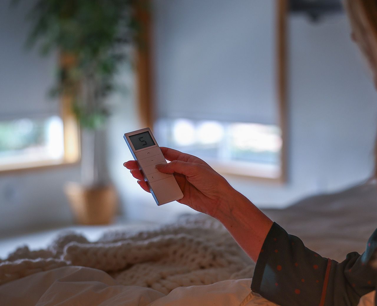 Hand holding UBlockout remote control in bed with motorized top down bottom up shades visible in background for convenient operation