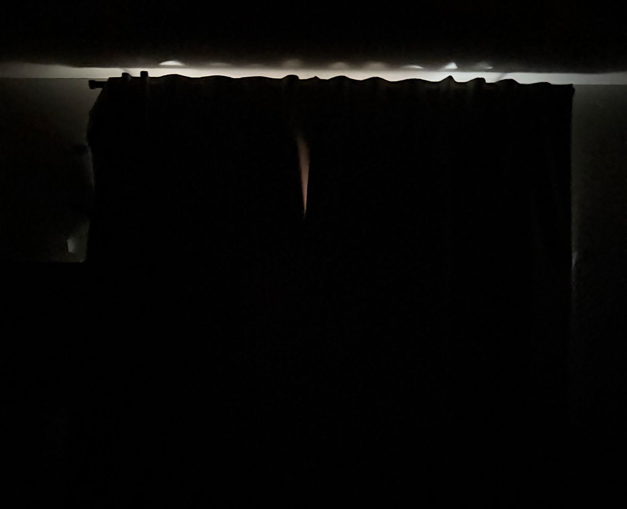 Blackout curtains at night showing light leaking over the top edge and through a center gap between curtain panels