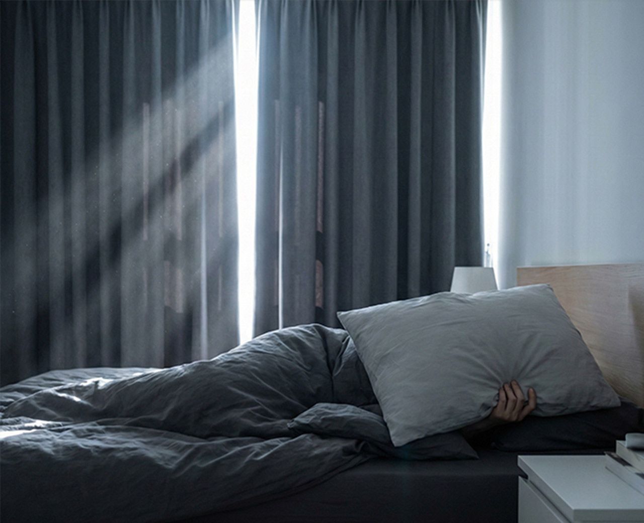 Person in bed covering face from light streaming through standard blackout curtains in bedroom