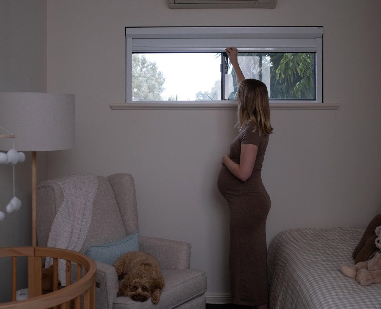 Pregnant woman adjusting blind in nursery that fails to fully cover window