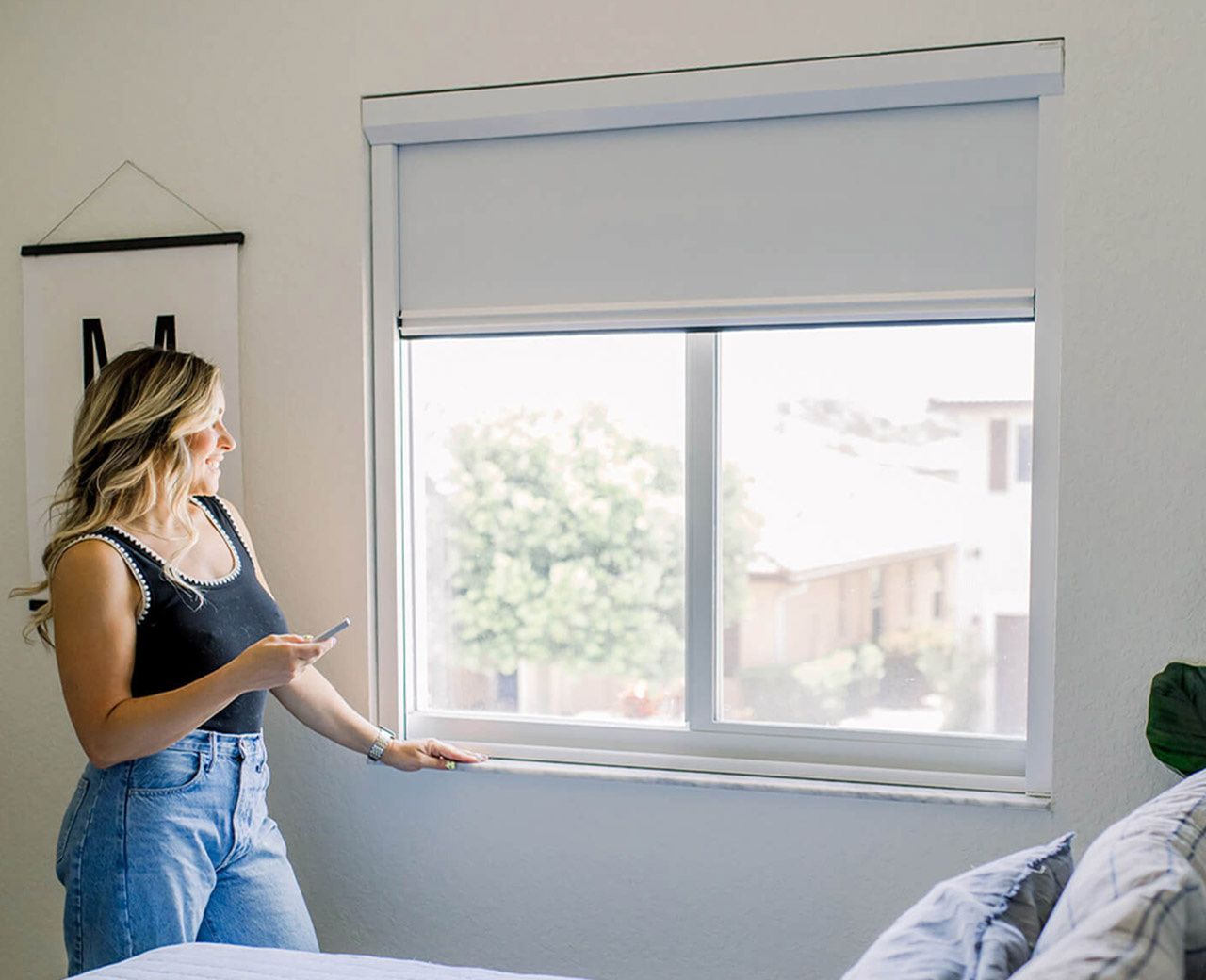 Woman using remote to control uBlockout roller shade on bedroom window