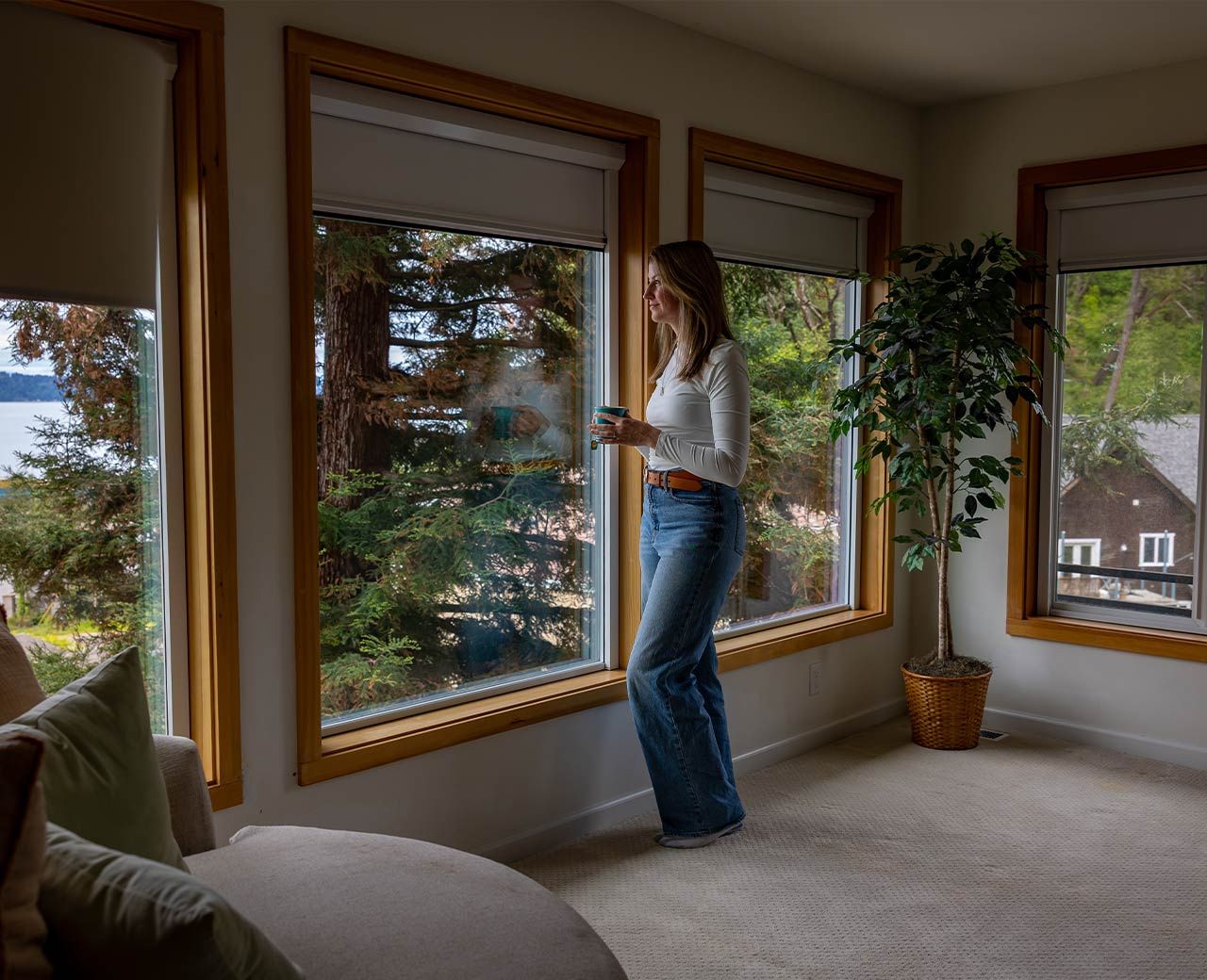 Woman standing by large windows with uBlockout roller shades partially lowered controlling natural light