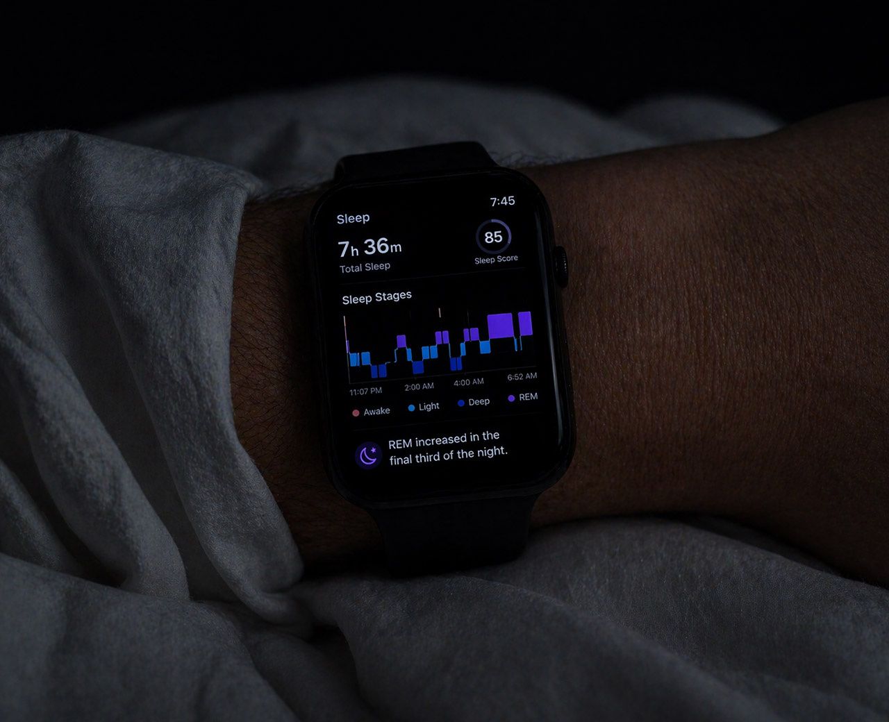 Sleep tracker on wrist glowing in dark bedroom showing REM sleep graph on screen
