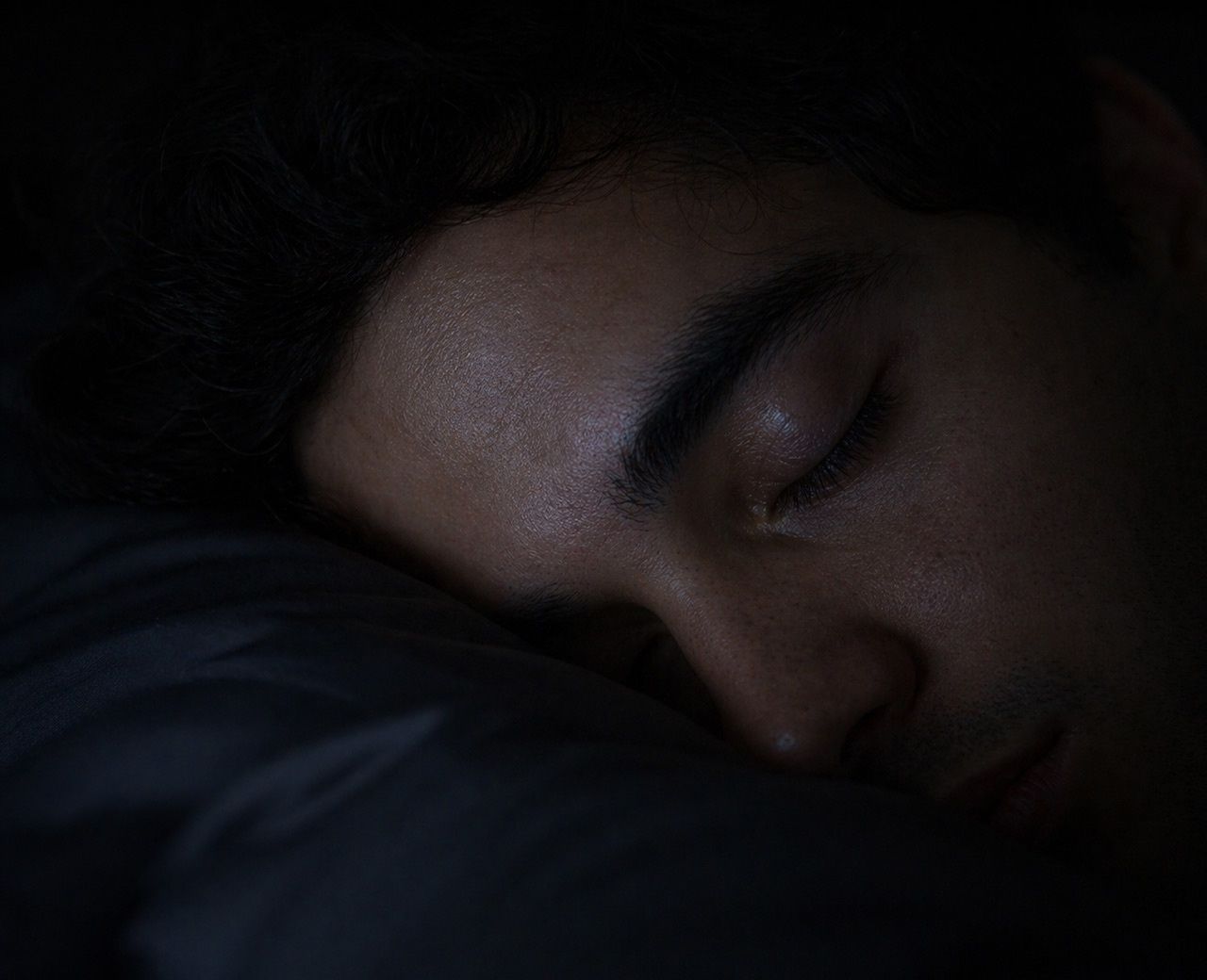 Close-up of sleeping face in dark room with subtle eye movement during REM sleep