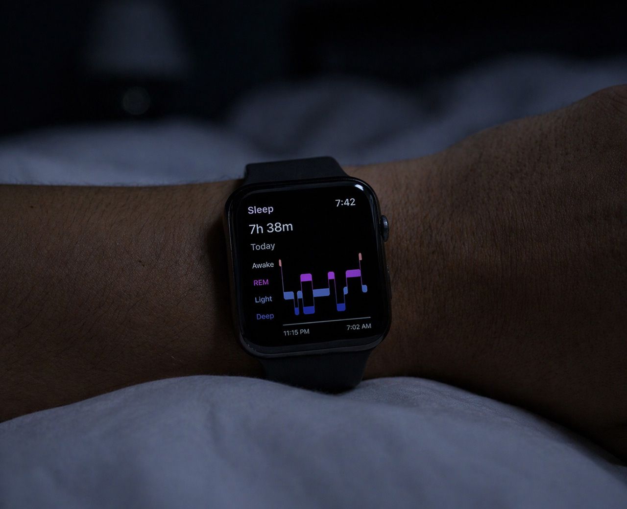 Sleep tracker on wrist showing sleep stages with highlighted REM band in dark bedroom