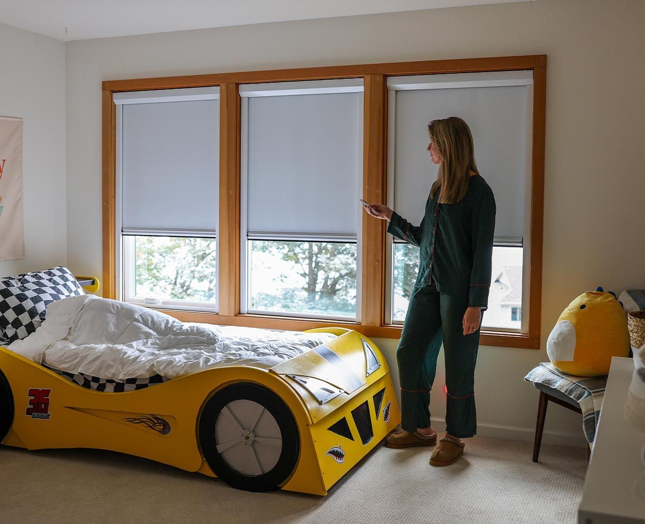 Woman using remote to control uBlockout shades on multiple windows in child’s bedroom