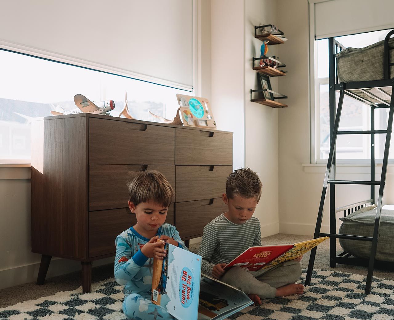 Two children reading books on floor beside window with uBlockout shade filtering daylight