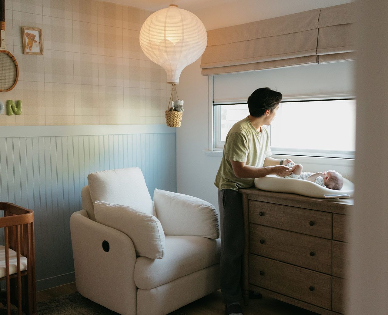 Father changing baby by window with uBlockout shade partially lowered filtering daylight