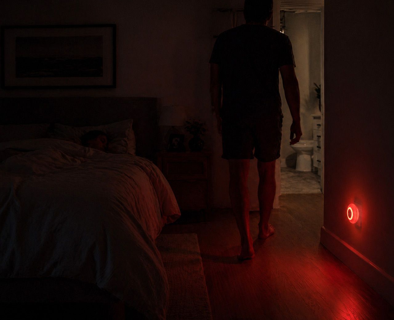Person walking through dark bedroom at night guided by dim red motion sensor night light
