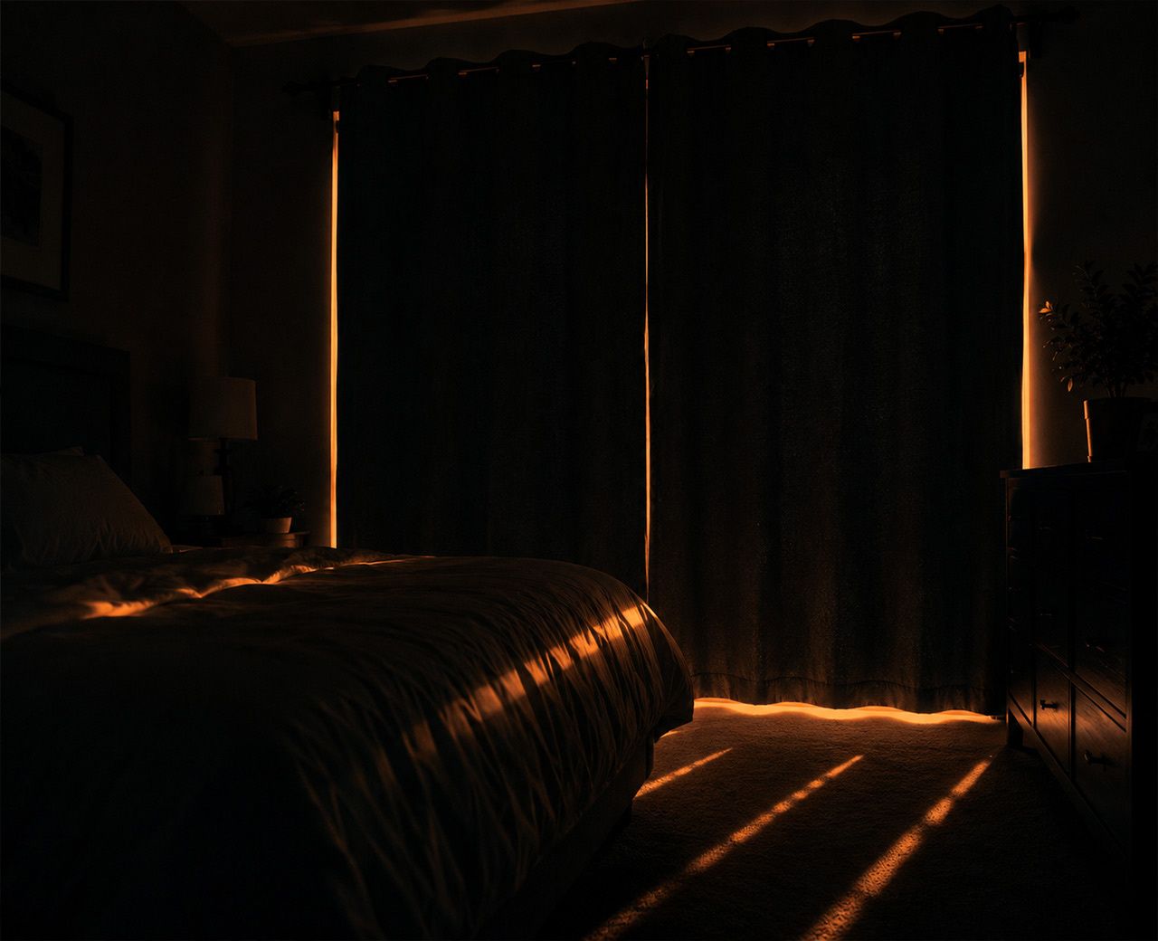 A dark bedroom at night with orange streetlight leaking through gaps around the curtains.