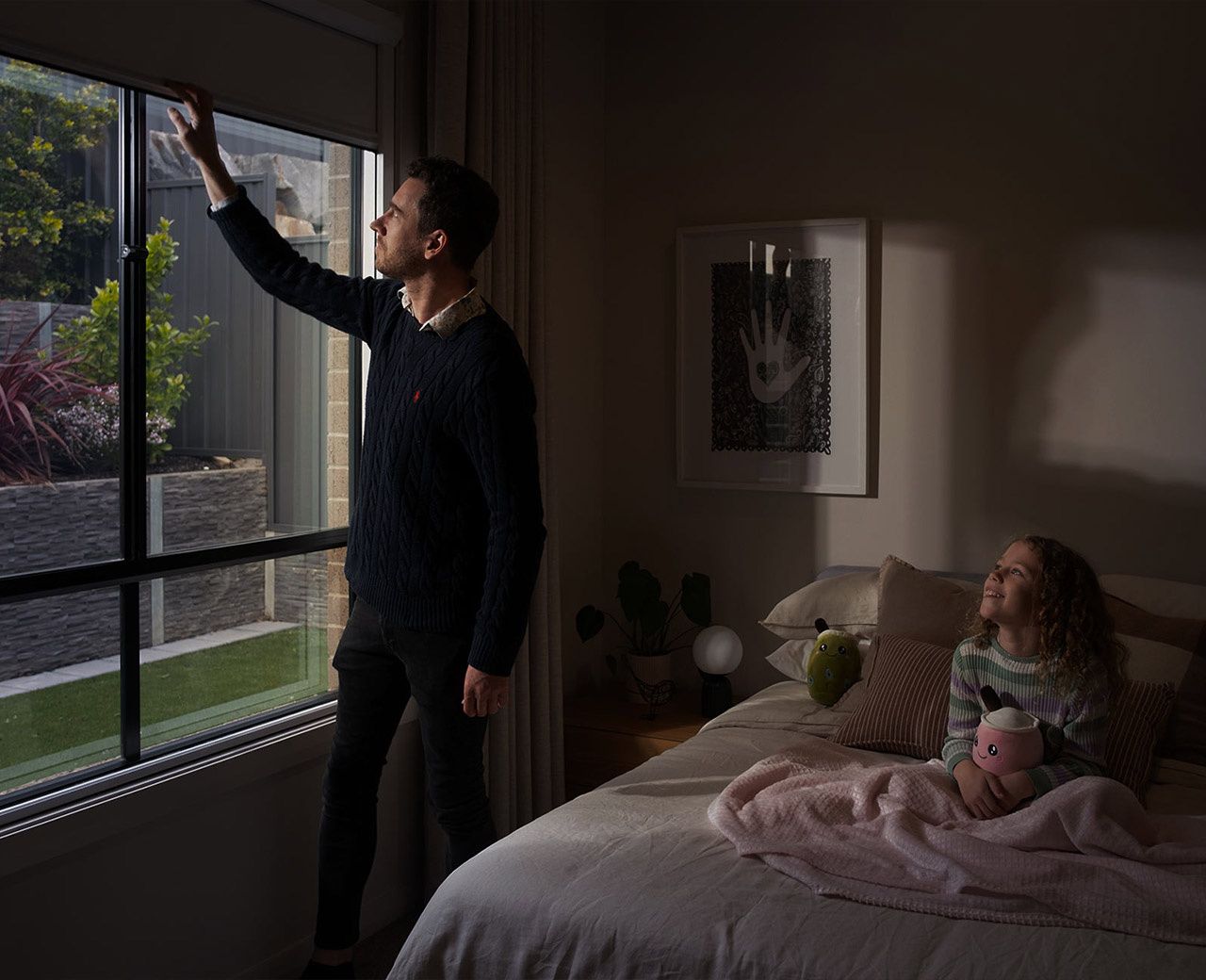 A dad pulling down a UBlockout blackout shade in his daughter's darkened bedroom at night.
