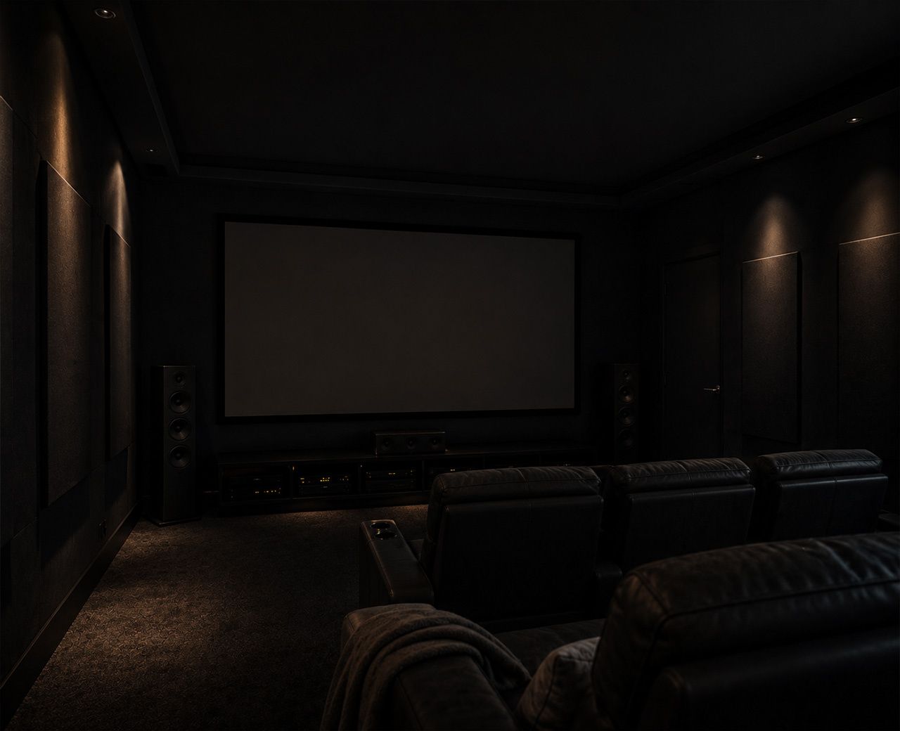 A dark home theater room with matte charcoal walls and faint LED indicator lights visible on electronics in the darkness.