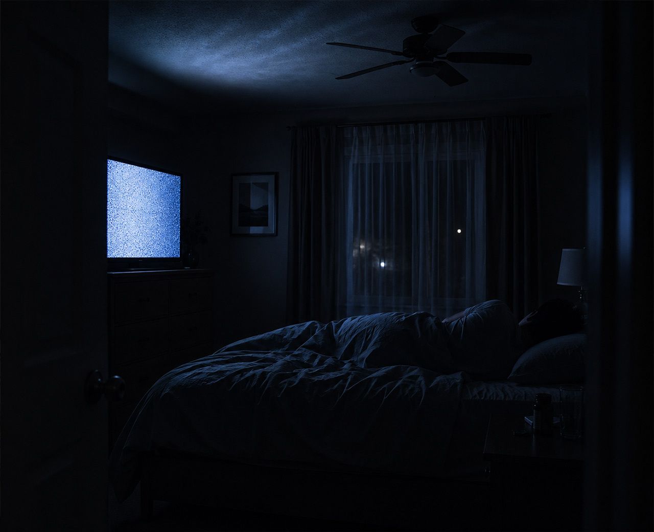 A dark bedroom at night with a television casting cold blue light across a person lying in bed.