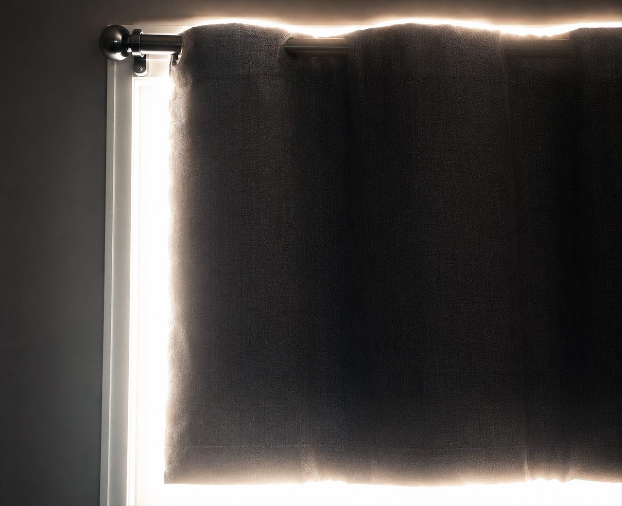  Intense midday sunlight blazing through gaps around all four edges of a bedroom curtain.