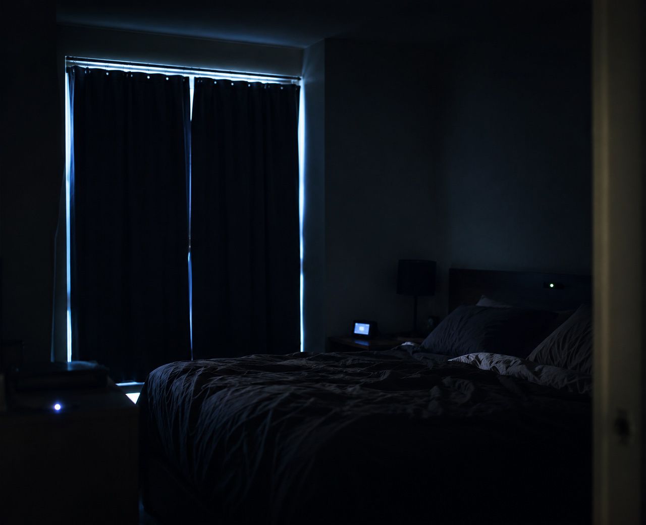Dark bedroom at night with unwanted light sources including streetlight glow through curtain gaps and LED device indicators
