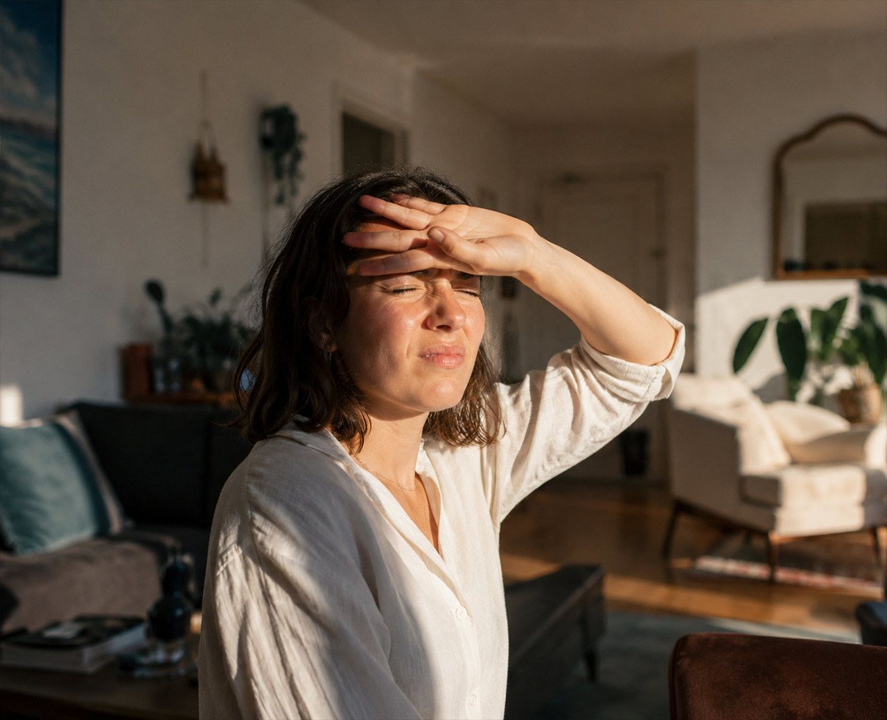 Person shielding their eyes with their hand as bright sunlight floods through an uncovered living room window