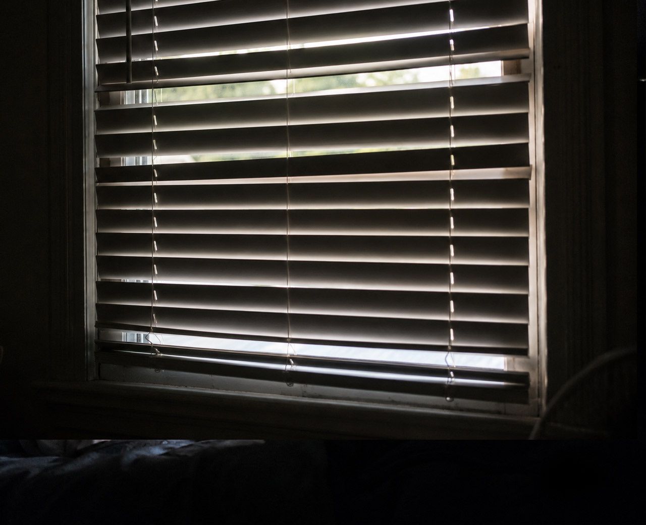 Standard slatted blinds closed on a window with visible light gaps between slats and at the edges