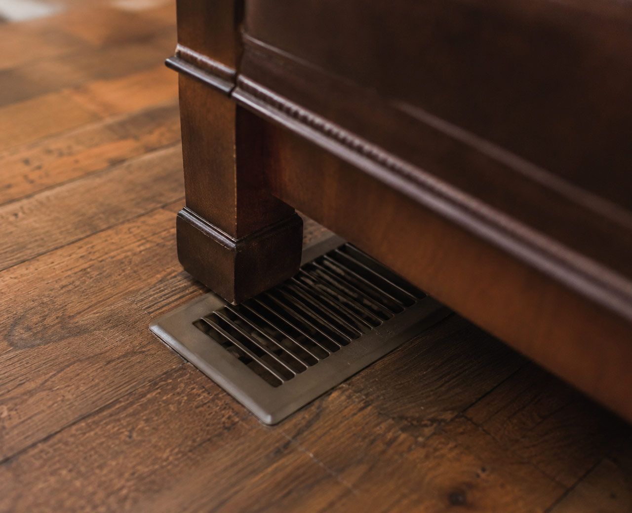 Floor air vent partially blocked by furniture leg preventing conditioned air from flowing into the room