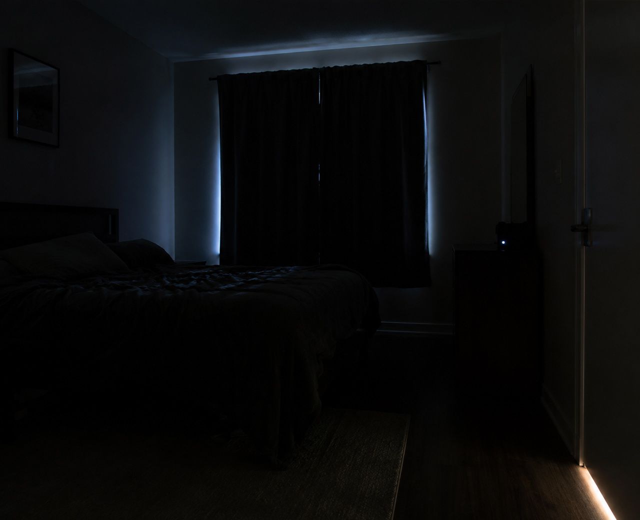 Dark bedroom at night with unwanted light sources including streetlight around curtain edges, a glowing LED standby light and light under the door