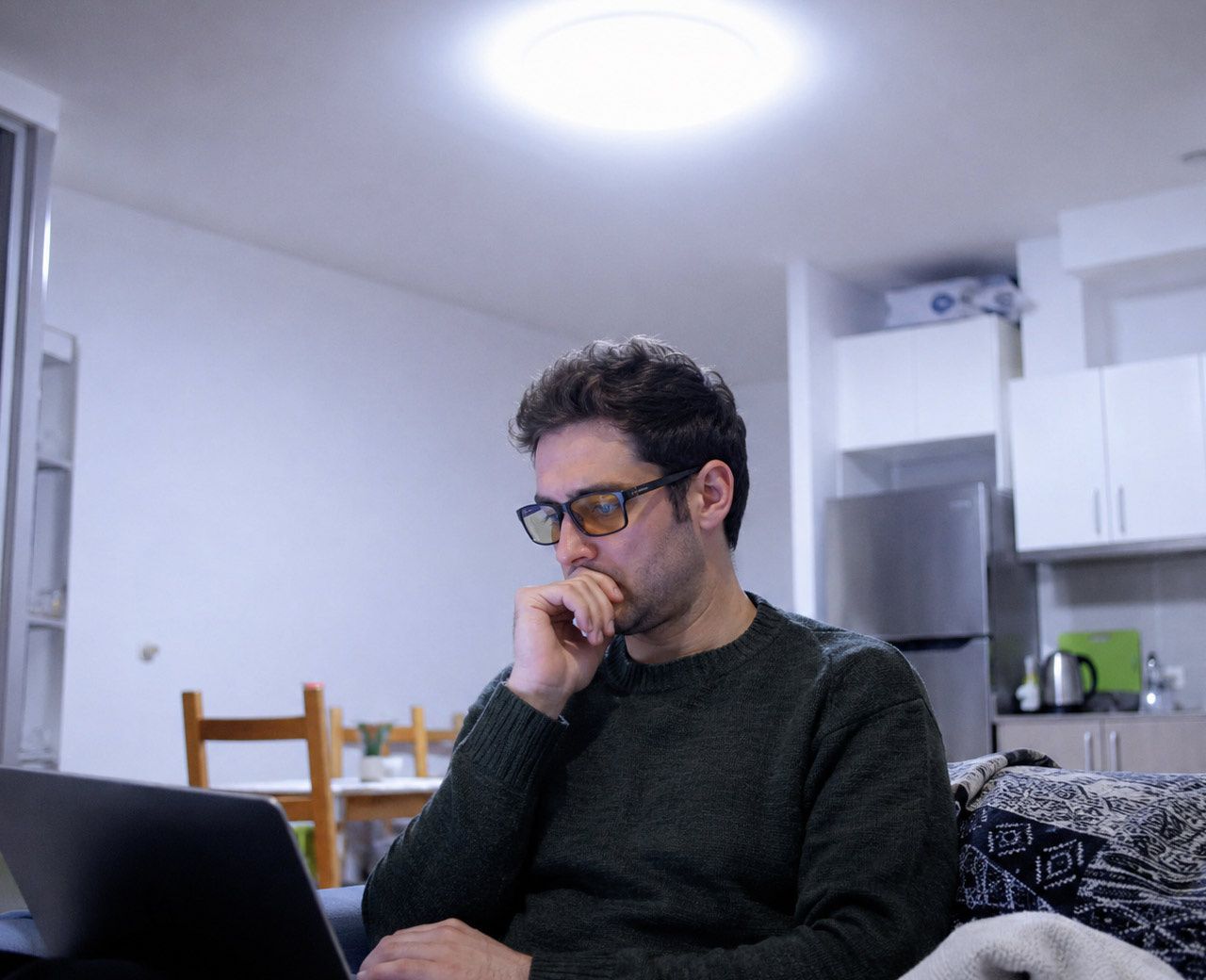 Person wearing blue light glasses sitting under bright cool-white overhead LED lighting in the evening