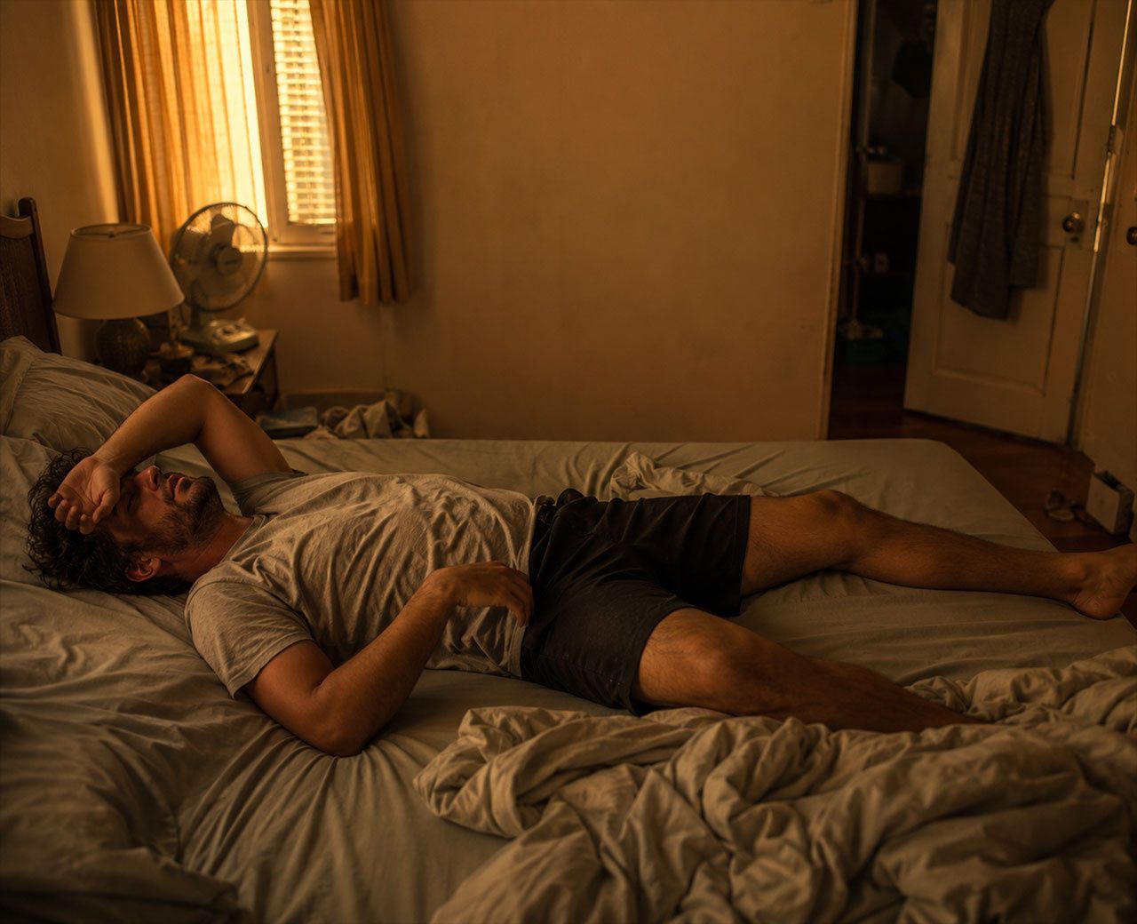 Person lying on top of kicked-off bed covers in a warm stuffy bedroom looking uncomfortable and unable to sleep