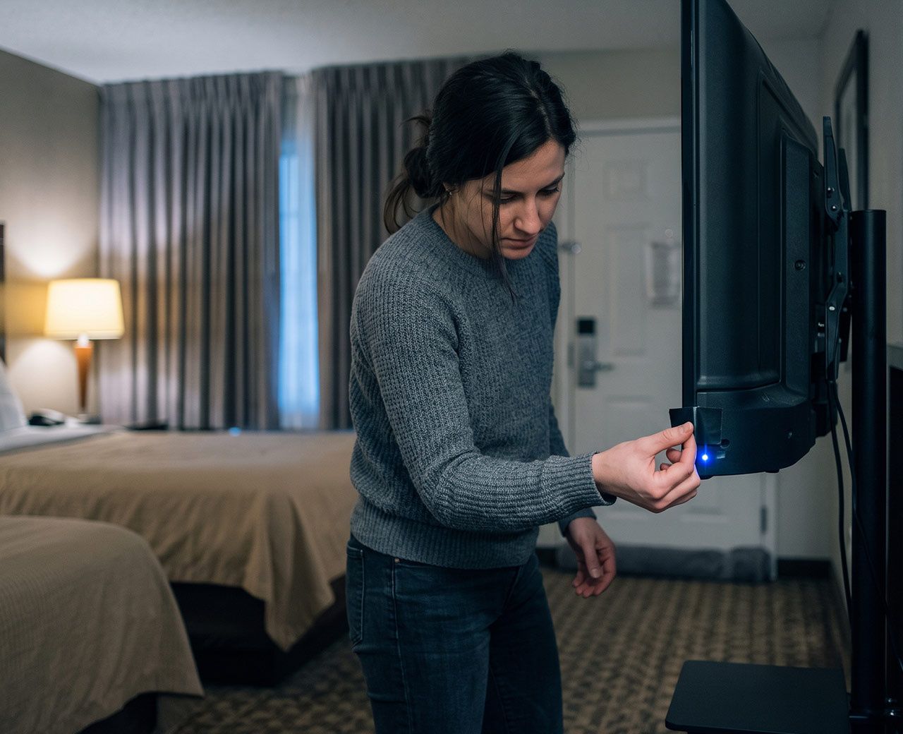 Traveler covering a glowing LED light on a hotel TV to make the room darker for sleep