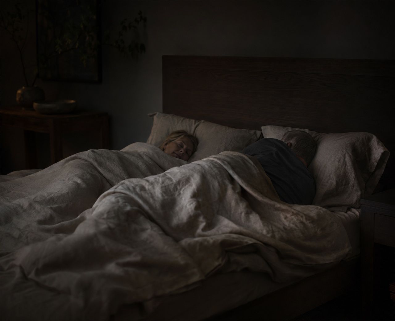 Older couple asleep in a dark bedroom with one person shifting position during the night