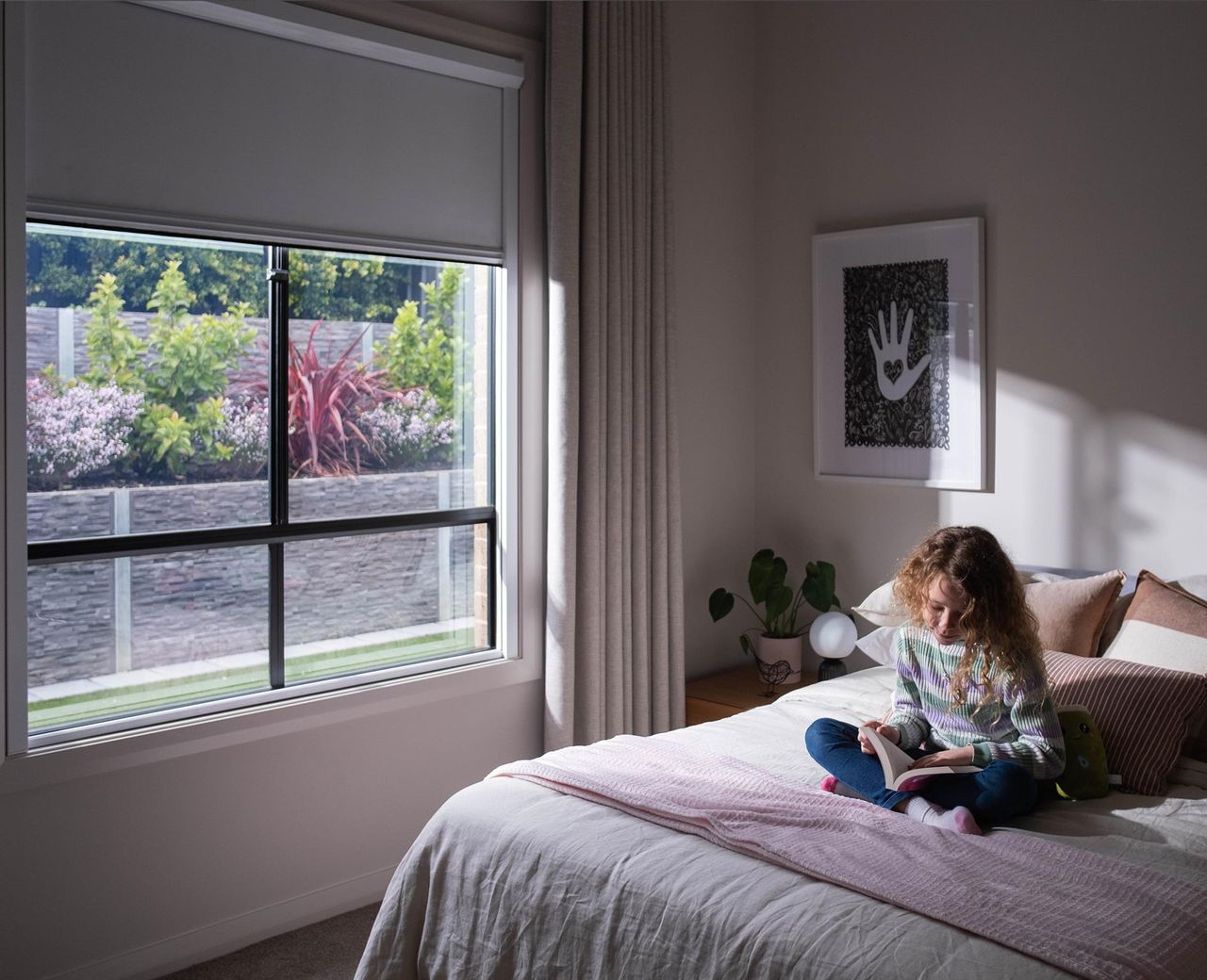 Child sitting on bed reading book with uBlockout shade partially raised letting in daylight