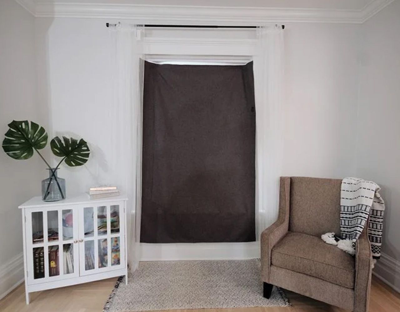 Sleepout portable blackout curtain installed on a bedroom window using suction cups with visible light gap at the top edge and sheer curtains hanging on either side