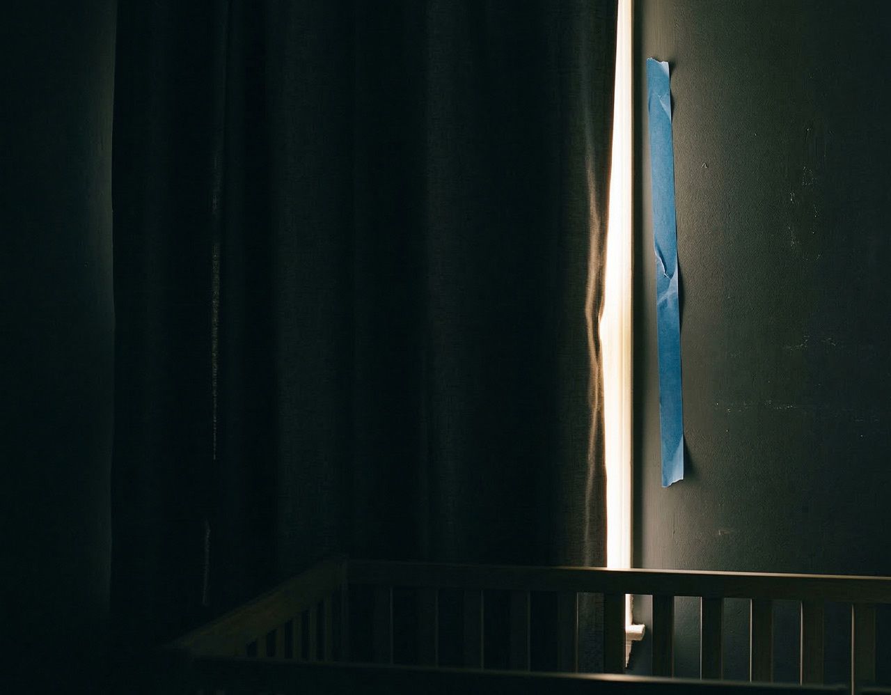 Light leaking through blackout curtain edge gap in nursery with painter's tape DIY fix peeling off the wall next to crib