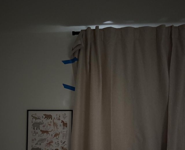 Failed DIY blackout hack showing blue painter's tape on curtain edges with light still leaking through gaps