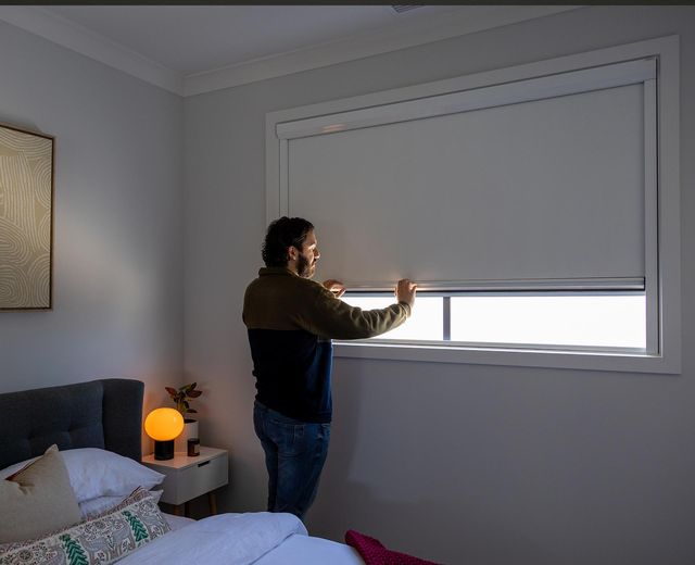Man adjusting UBlockout blackout shade in bedroom showing sealed aluminum side tracks that block 100% of light