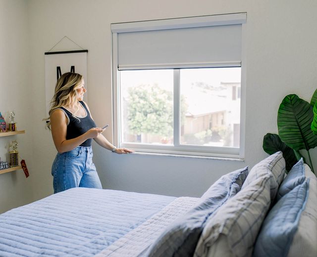 Woman controlling motorized blackout shades with remote