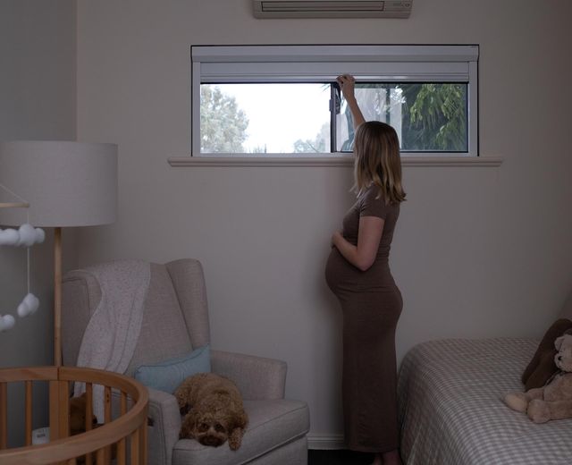 Pregnant-mother-pulling-down-UBlockout-shade-in-nursery,-daylight-visible-through-window-before-shade-reaches-complete-blackout-position..jpg