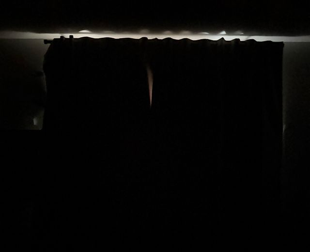 Thin strip of bright white light leaking above dark curtains where the rod meets the ceiling