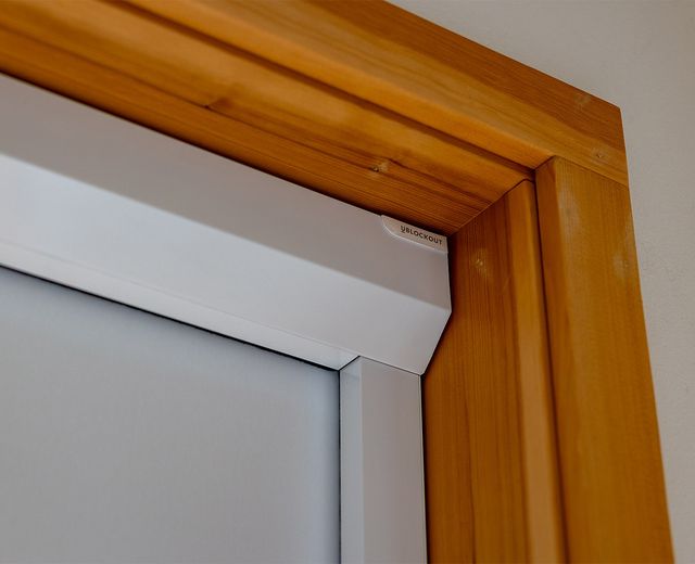 Close-up of a UBlockout motorized shade corner bracket with sealed aluminum side track flush against a timber window frame