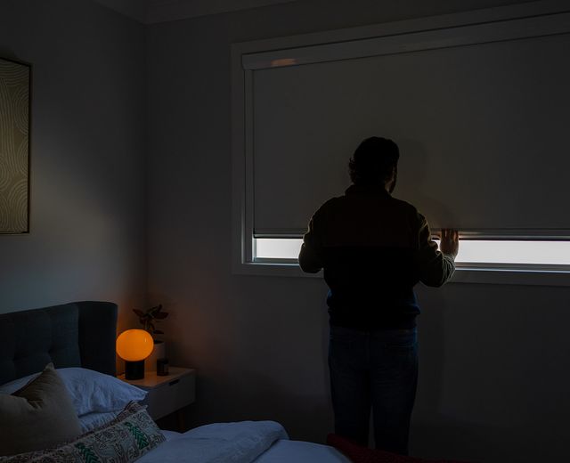Person silhouetted in a dark bedroom observing the darkness of a UBlockout shade