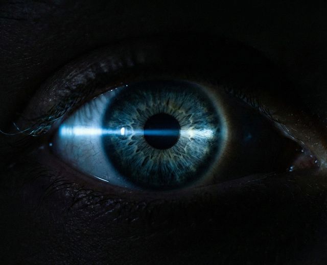Close-up of human eye with light beam reflecting off iris in darkness