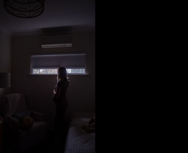 Woman standing in near-total darkness in bedroom with UBlockout shade fully blocking exterior light