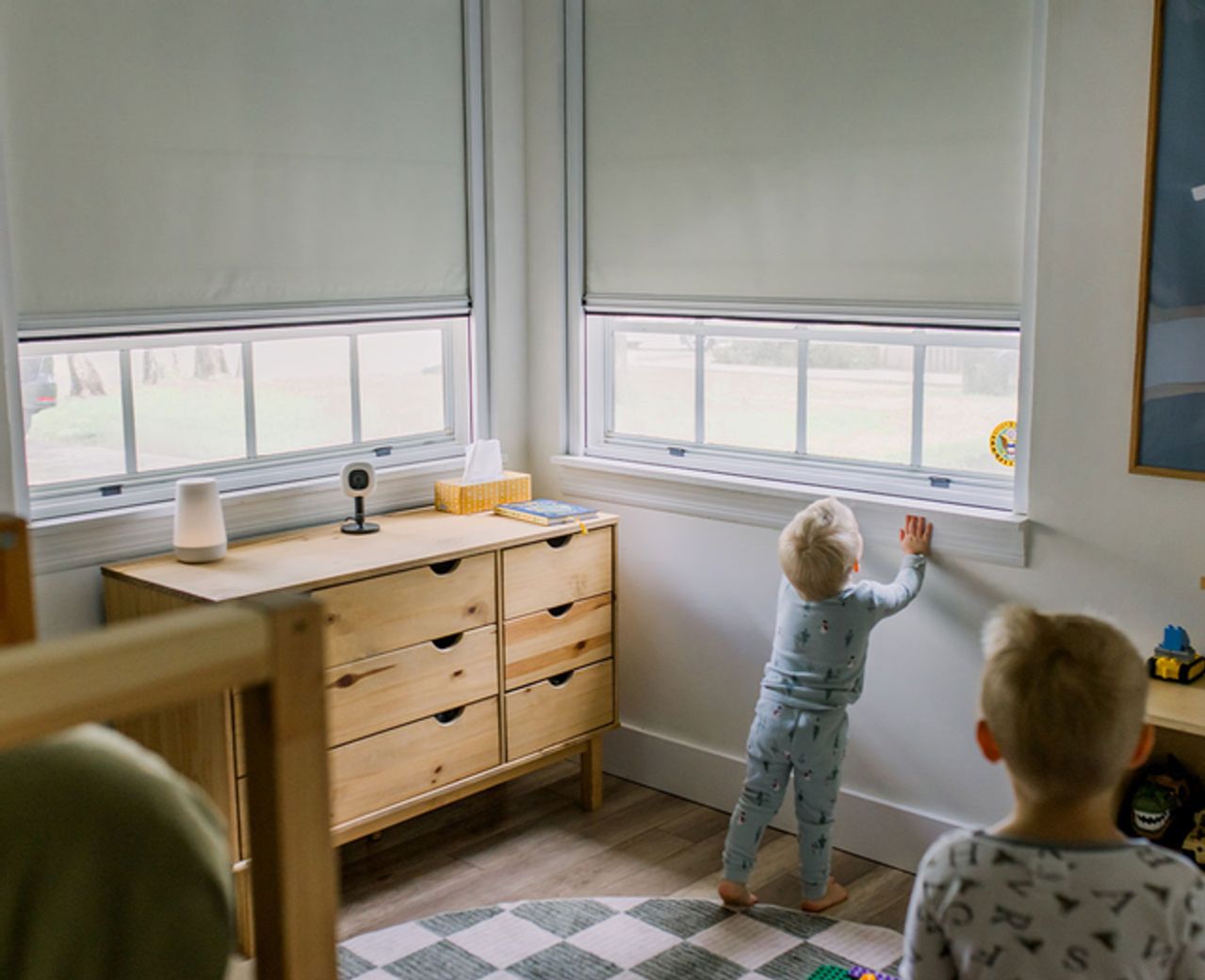 Two young children in pajamas standing at windows fitted with white UBlockout shades