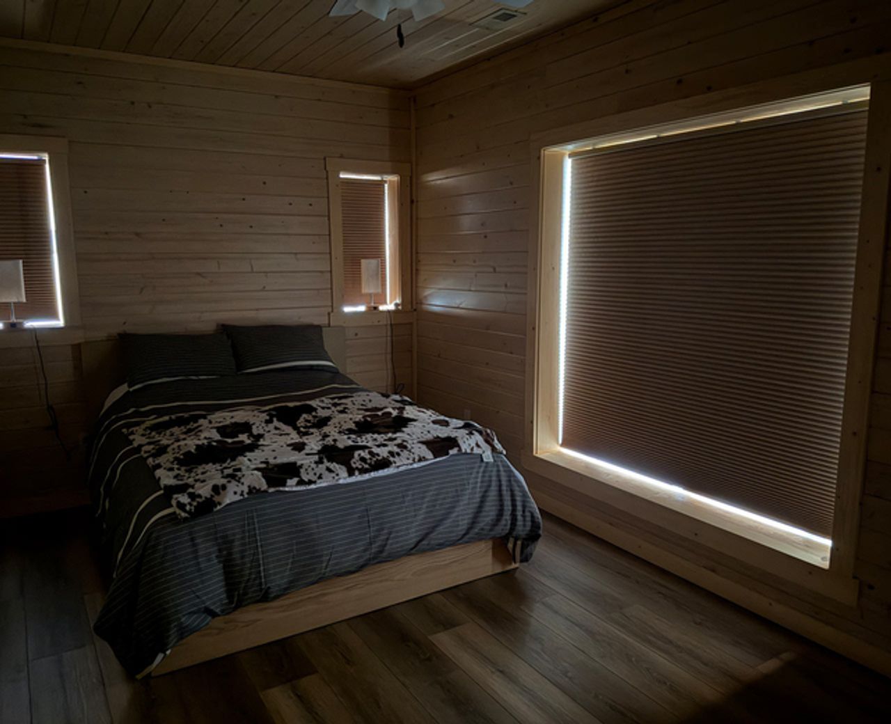blog-image-shade-leak.Rustic wood-paneled bedroom with bright light leaking around the edges and bottom of honeycomb blinds on multiple windows