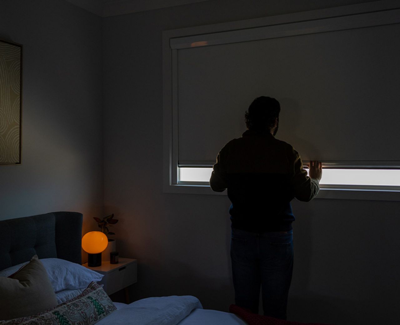 Person silhouetted in a dark bedroom observing the darkness of a UBlockout shade