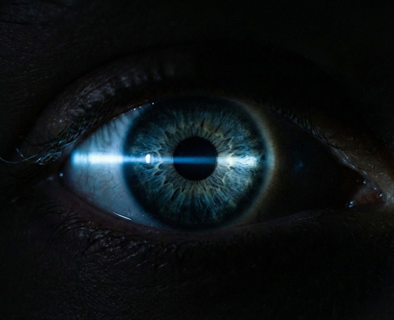Close-up of human eye with light beam reflecting off iris in darkness