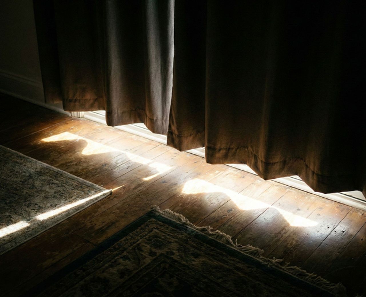 Morning light bleeding under blackout curtains onto hardwood floor and rug