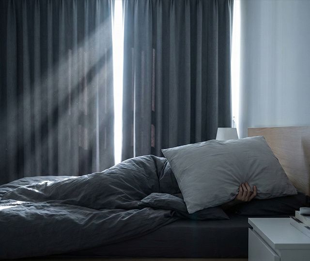 Person-in-bed-covering-face-with-pillow-while-morning-light-streams-through-gaps-in-room-darkening-curtainsTo-run-code,-enable-code-execution-and-file-creation-in-Settings-)-Capabilities. copy.jpg