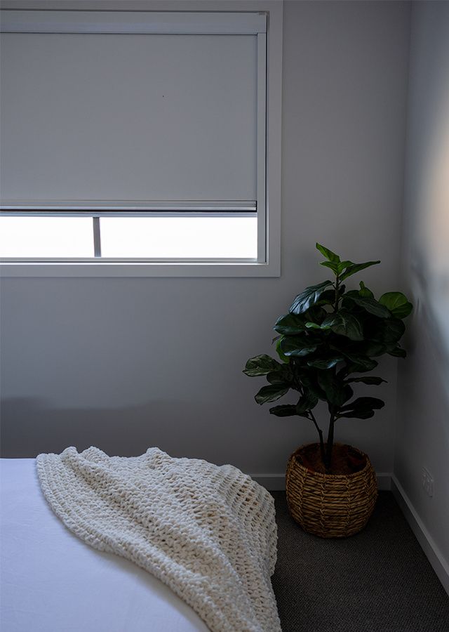 Room darkening roller shade in bedroom showing light passing through fabric and visible gap at the bottom of the window